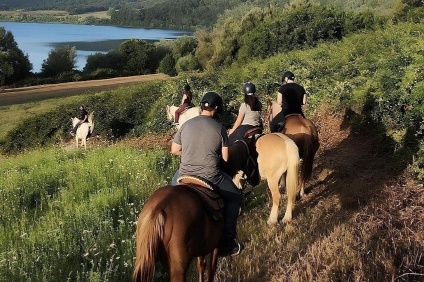En gruppe mennesker rider på heste ad en sti med en sø i baggrunden. 4