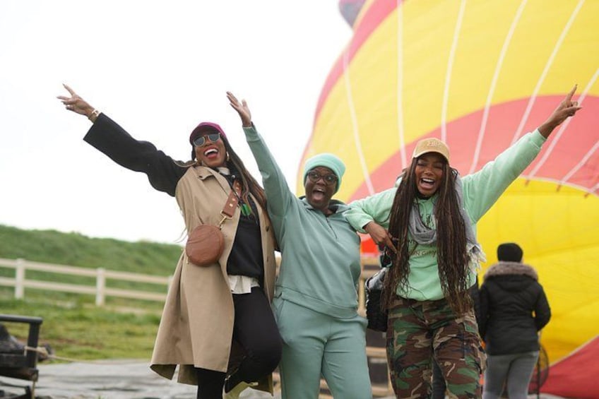 Three people with arms outstretched near a large hot air balloon. 2
