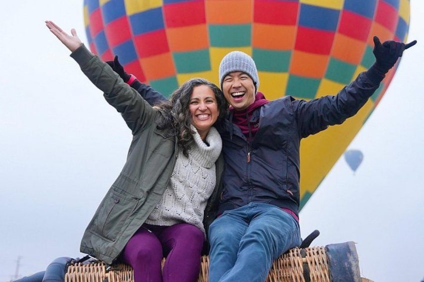Dos personas sentadas en una plataforma, con un globo aerostático colorido al fondo. 1