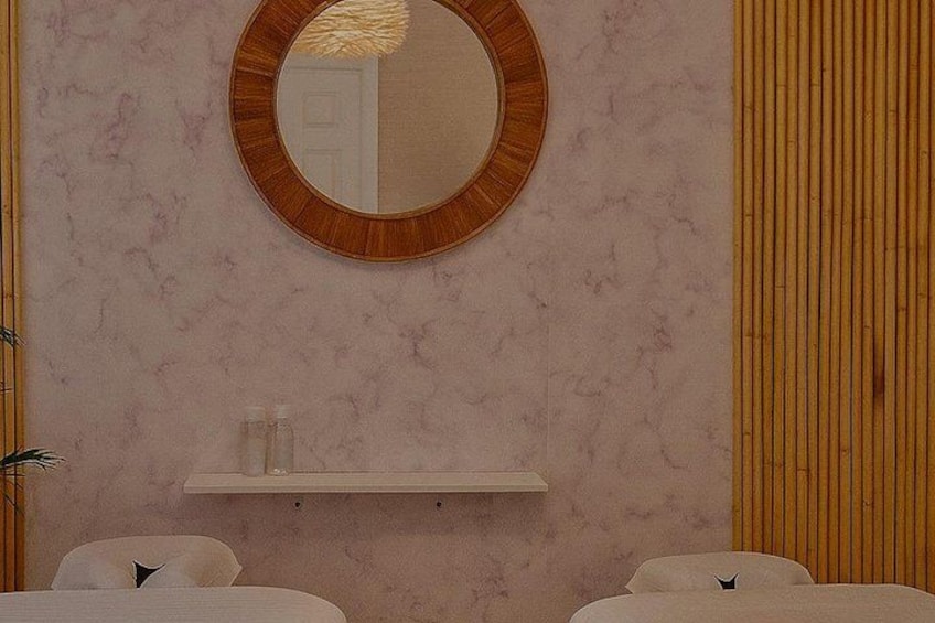 A spa room with a round mirror, a shelf, and two white chairs with cat symbols. 5