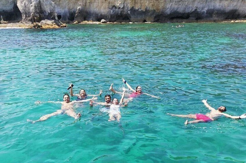 People swimming in clear turquoise water with rocky cliffs in the background. 4