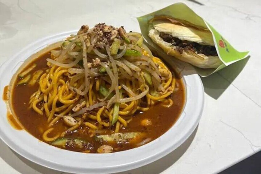 A bowl of noodles with vegetables and a sandwich on a white table. 4