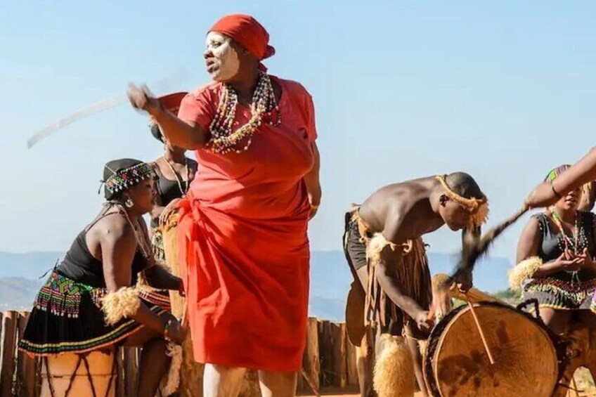 Une personne vêtue d’une robe rouge joue du tambour, entourée d’autres personnes portant des costumes traditionnels. 5