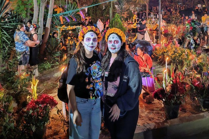 Two people posing in a cemetery decorated with flowers and candles. 2