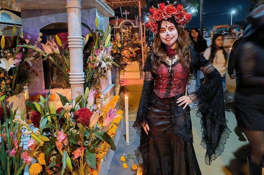 A person in a gothic costume with a floral headpiece standing in front of a decorated altar with flowers. 1