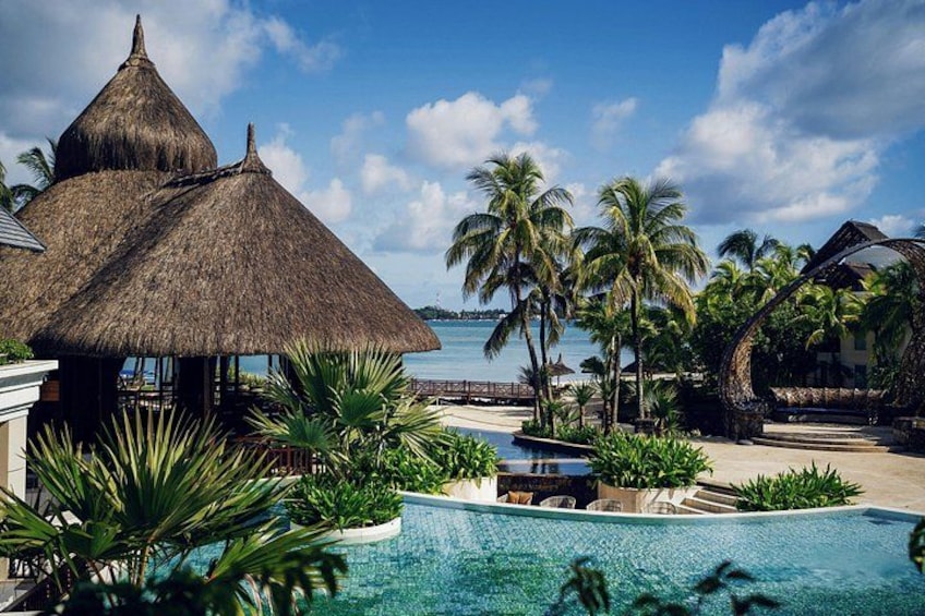 A tropical resort with a swimming pool, palm trees, and thatched-roof structures. 2