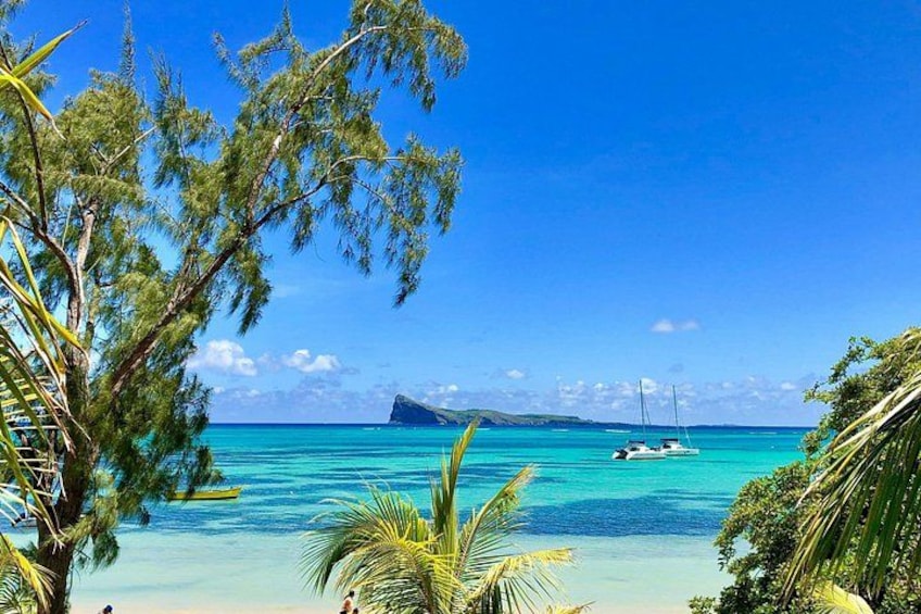 A tropical beach with clear turquoise waters, a small island in the distance, and a boat anchored near the shore. 1