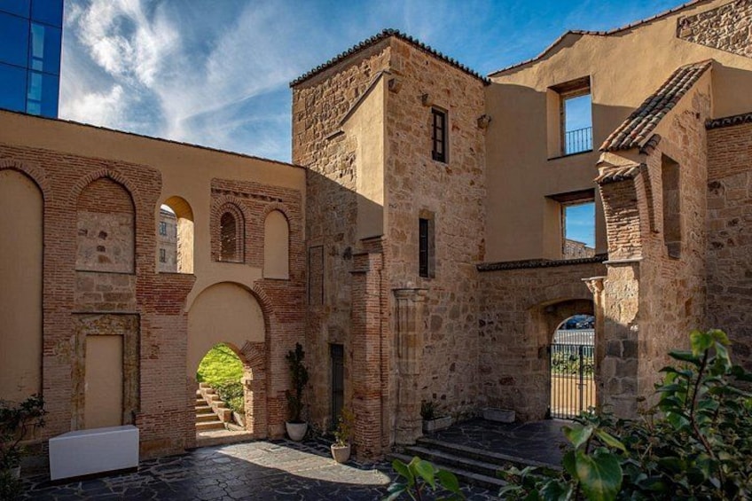 A courtyard with stone buildings, an arched entrance, and potted plants. 5