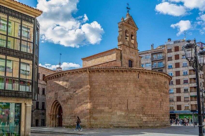 A historic stone building with a bell tower, surrounded by modern buildings and a clear sky. 3