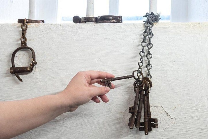 A hand holding a key near a white wall with a metal chain and a padlock. 5
