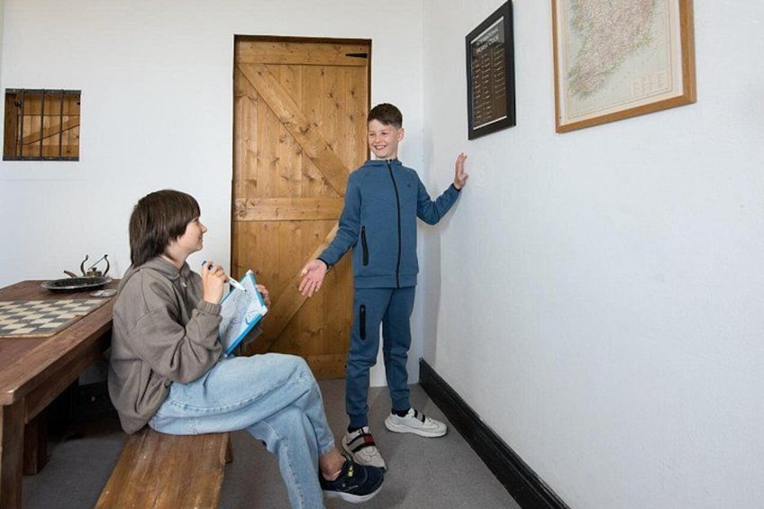 Two people in a room with a wooden door, a framed map, and a chessboard on a table. 2