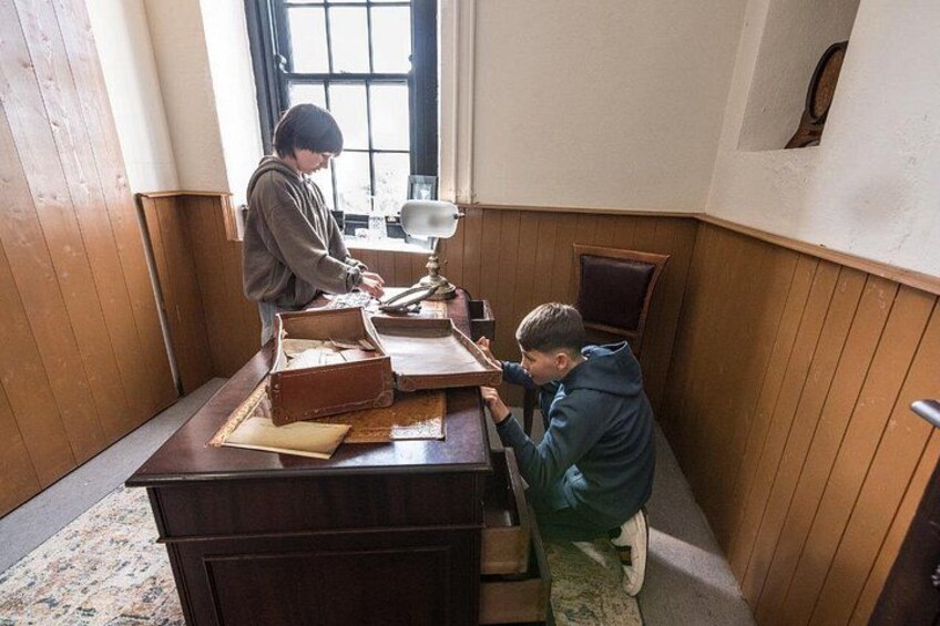 Two people in a room with wooden walls and a table, one person is standing and the other is sitting. 3