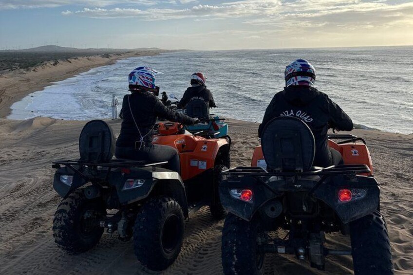 Three people on ATVs on a sandy beach with the ocean in the background. 3