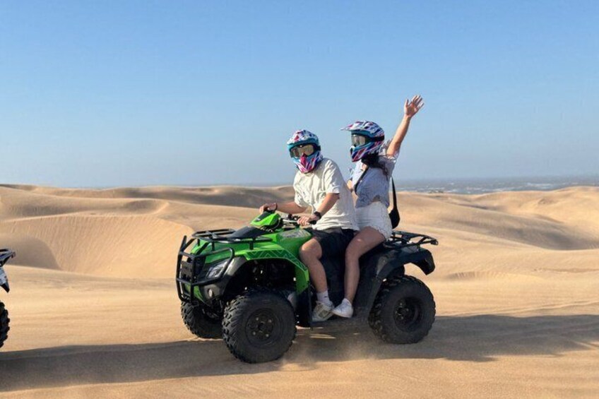 Two people on a green quad bike in a desert with sand dunes. 4