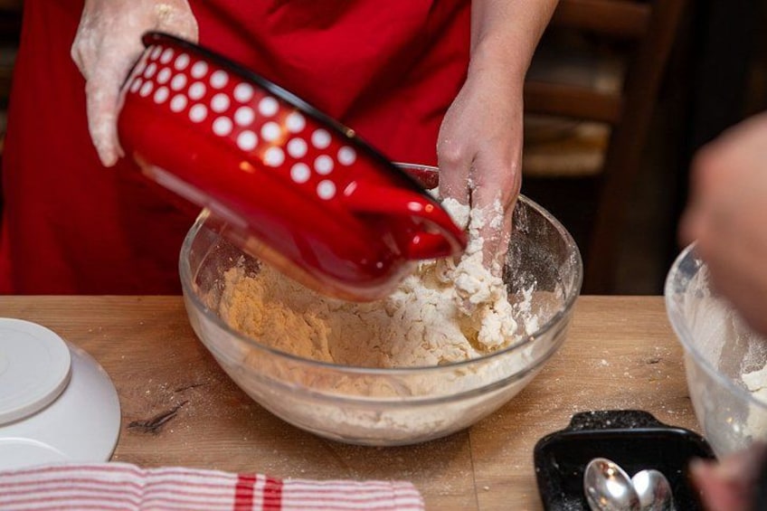 A person pouring a red container into a glass bowl on a wooden table. 1