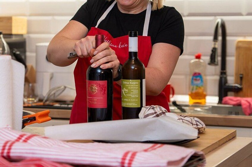 A person wearing a red apron, holding two bottles of wine, with a kitchen counter in the background. 2
