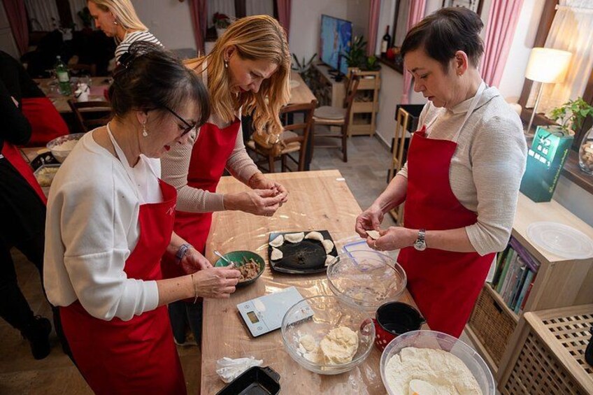 Three people in a kitchen preparing food, with ingredients and utensils on the table. 4