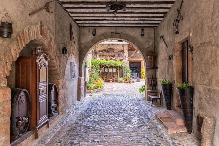 Un callejón adoquinado con arcos, barriles de madera y macetas con plantas. 2