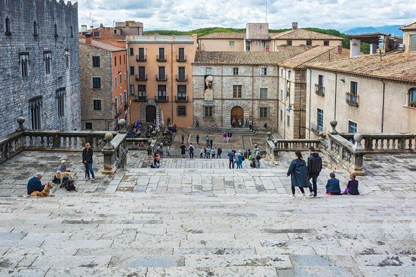 Una plaza histórica con edificios de piedra, una escalera central y gente caminando y sentada. 4