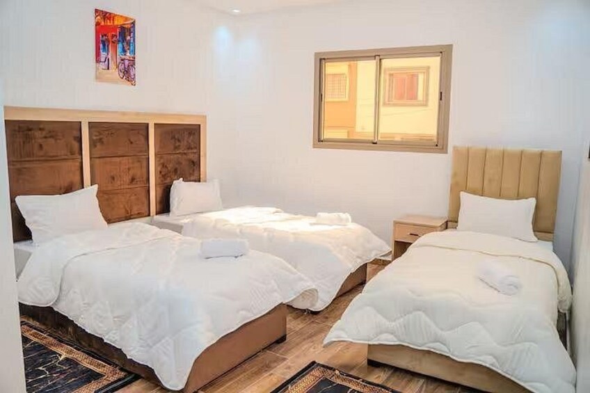 A hotel room with two beds, a wooden headboard, a window, and a colorful painting on the wall. 3