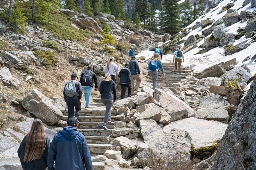 Hikers ascending a rocky mountain trail surrounded by snow-covered terrain and sparse vegetation. 4