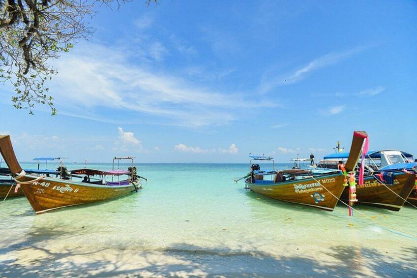 Twee houten boten aan een strand met helder turquoise water en een strakblauwe lucht. 3