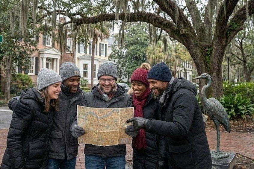 A group of people examining a map outdoors with trees and a statue in the background. 1