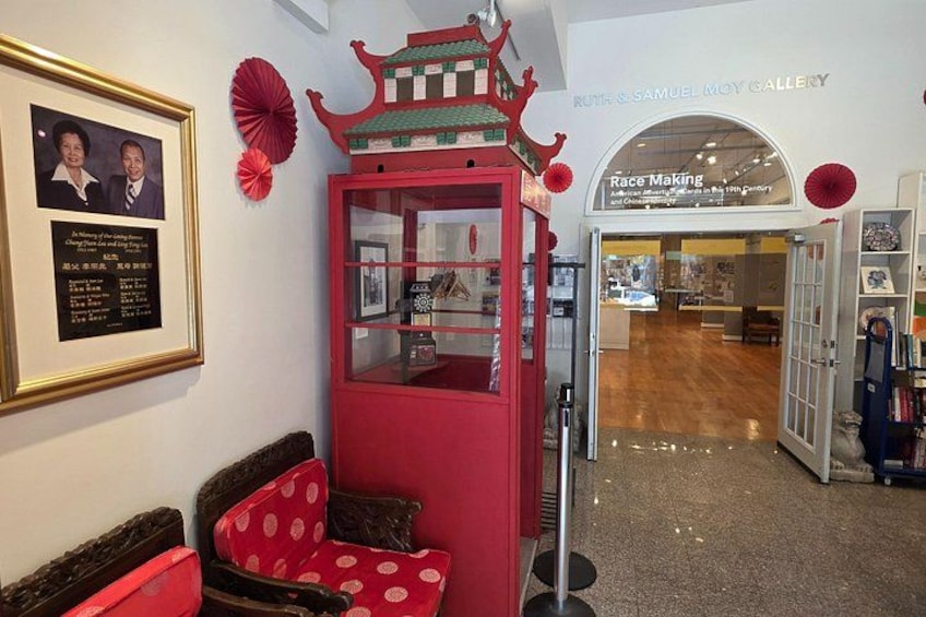 En konstgalleris interiör med en röd monter, en inramad tavla och en skylt för Ruth & Samuel Moy Gallery. 1
