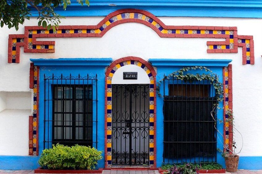 A building with blue and red tiled patterns, black metal gates, and a potted plant. 5