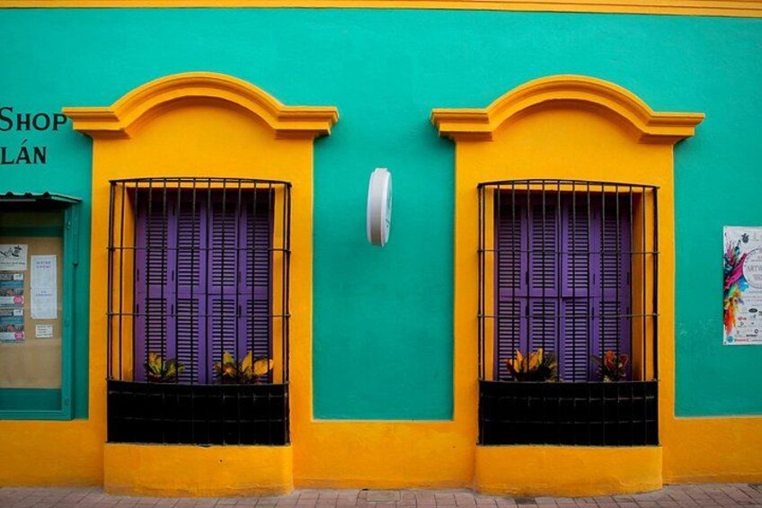 A building with two windows, each with a purple shutter and a yellow arch above. 3