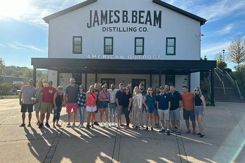 En grupp människor som står framför James B. Beam Distilling Co., American Outpost. 1