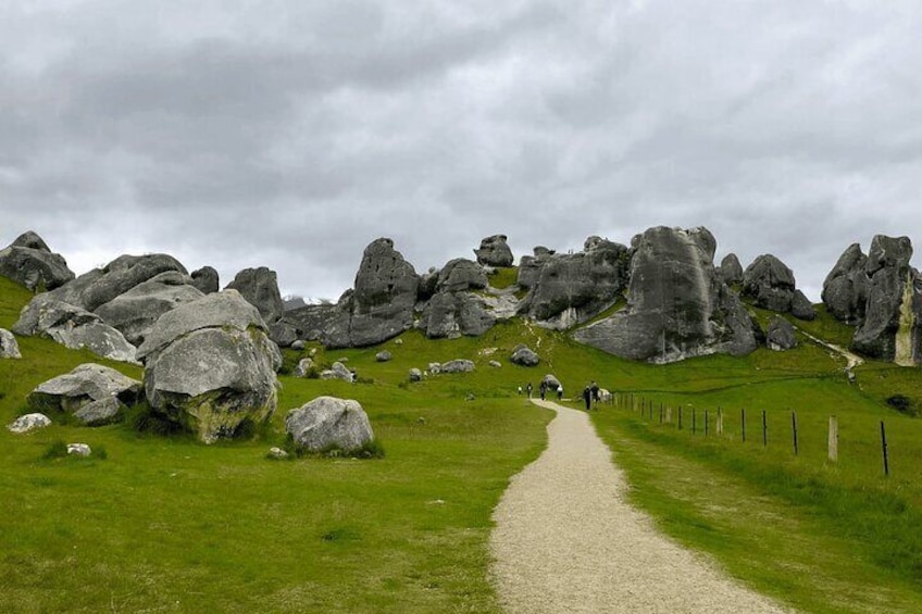 A gravel path leading through a grassy area with large boulders and a fence along the side. 1