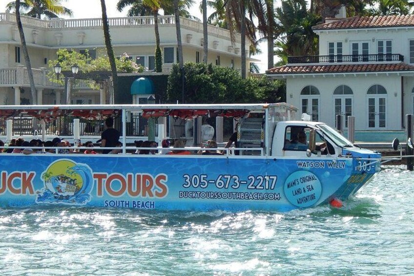 Ein blaues Tourboot namens 'Watson on Willy' mit 'Duck Tours South Beach' Branding liegt an einem Steg, im Hintergrund sind Gebäude und Palmen zu sehen. 1