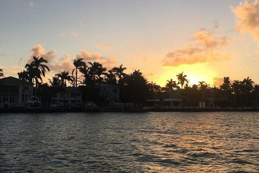 A sunset over a body of water with palm trees and buildings in the background. 2