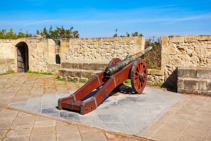 A historical cannon on a stone platform with a stone wall and a gate in the background. 3