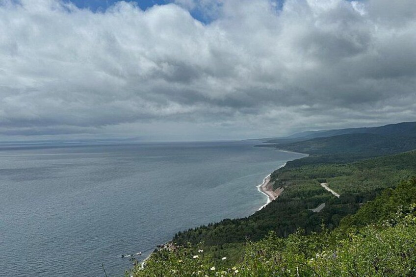 A coastal landscape with a beach, forested hills, and a cloudy sky. 5