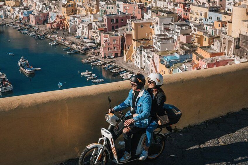 En kuststad med färgglada byggnader, en hamn med båtar och en person som kör motorcykel. 4