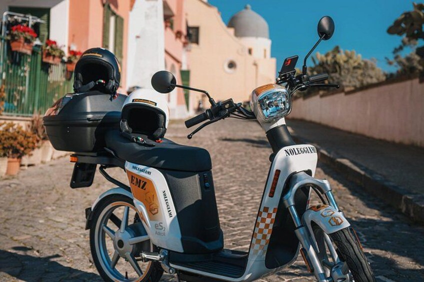 En vit och svart scooter med en hjälm fastspänd på pakethållaren, parkerad på en kullerstensgata. 3