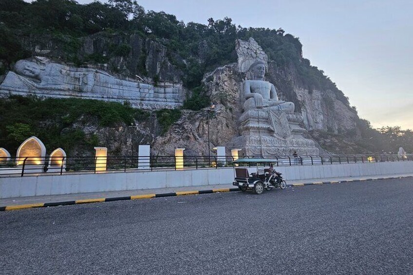 A large reclining Buddha statue on a cliff, a road with a motorcycle, and a guardrail with lights. 5
