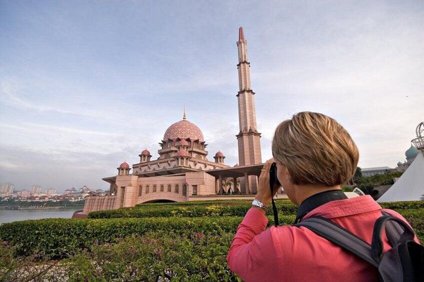 A person taking a photo of a large, pink-domed building with a tall minaret. 2