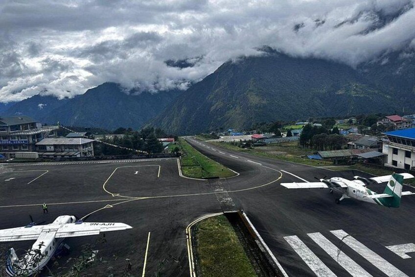 An airport runway with airplanes, buildings, and mountains in the background. 5