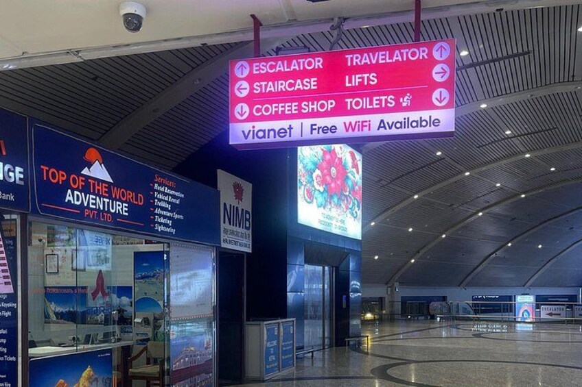 An airport terminal with signs for escalator, travelator, staircase, lifts, coffee shop, and toilets. 2