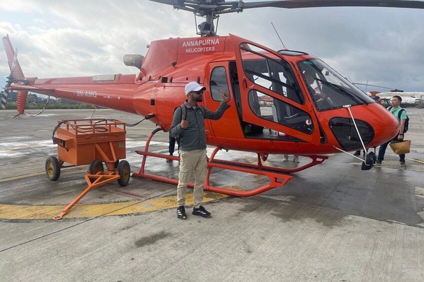 A red helicopter with 'ANNAPUR' written on it, a man standing next to it, and a cart. 1