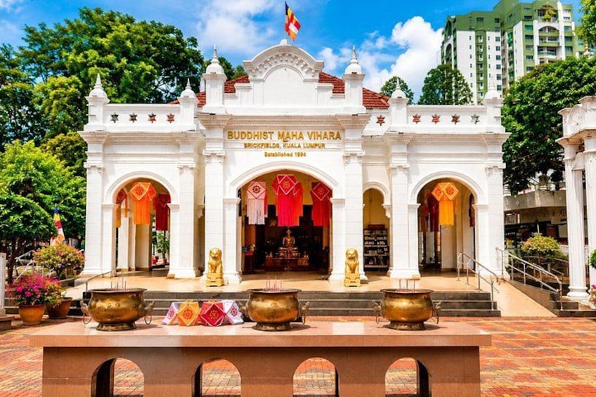 A Buddhist Mahavihara temple with a white facade, golden statues, and a flag. 4