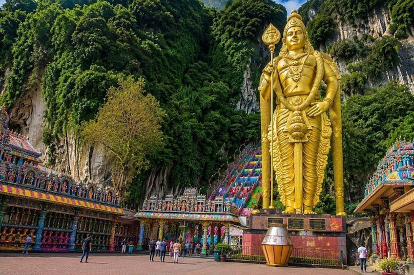 A large golden statue in a temple complex with colorful architecture and lush greenery. 1