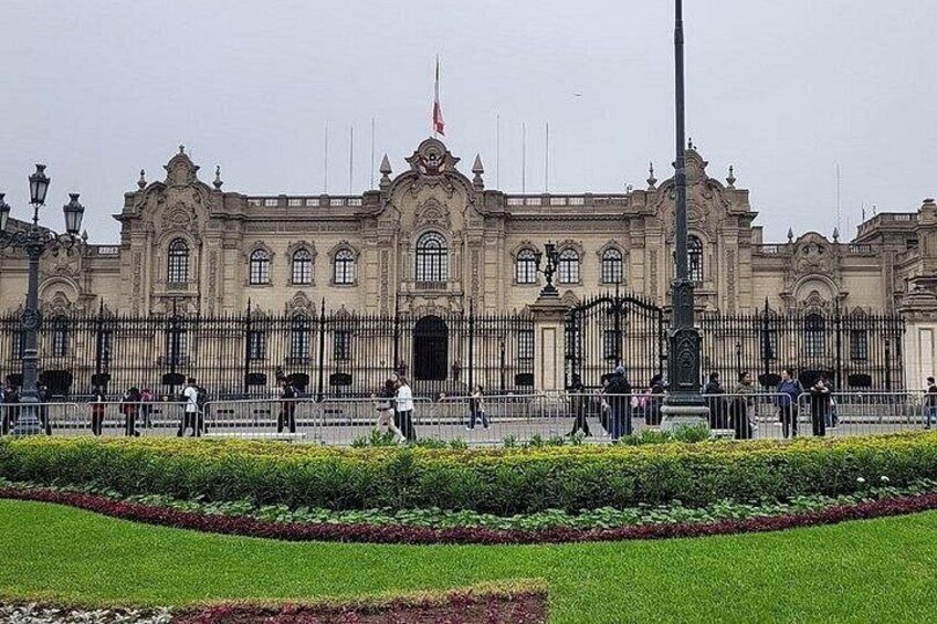 A large, ornate building with a flag, surrounded by a manicured garden and a fence. 2