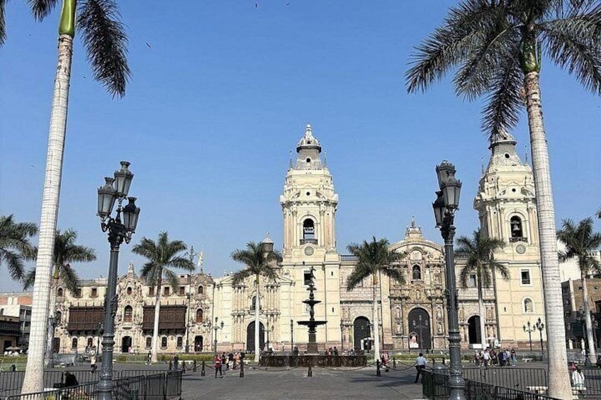 A historic cathedral with two towers, palm trees, and a clear sky. 5