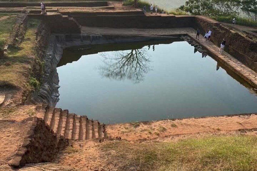 A large, rectangular water body with a stepped embankment leading to it, surrounded by dry land and a few people. 2