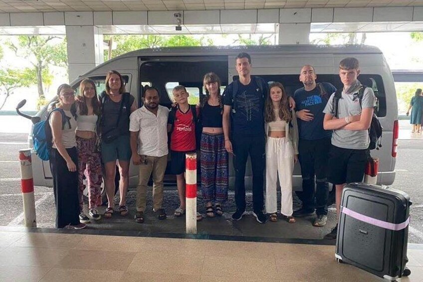 A group of people standing in front of a van at a parking area. 5