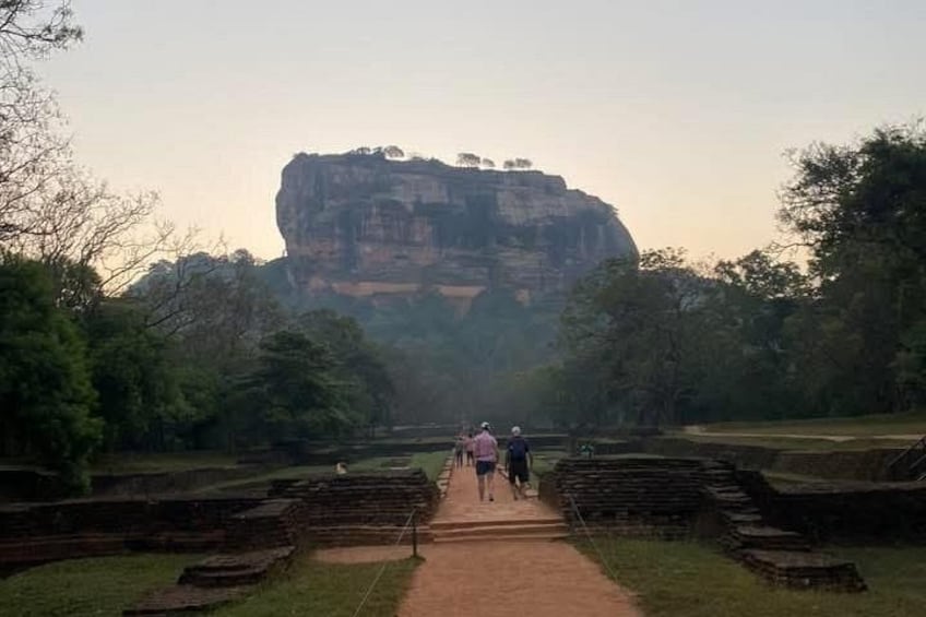 A pathway leading to a large rock formation with people walking towards it. 1